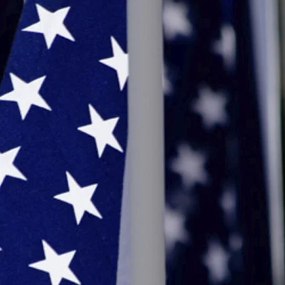 Close-up image of two American flags with white stars on a blue field, positioned side by side.