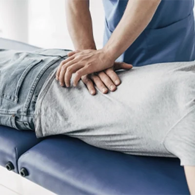 Patient lying on a padded treatment table while a practitioner applies hands-on pressure to the lower back area.