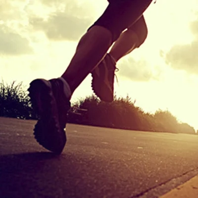Low-angle outdoor photo showing a person running on a paved road with athletic shoes during sunset lighting.